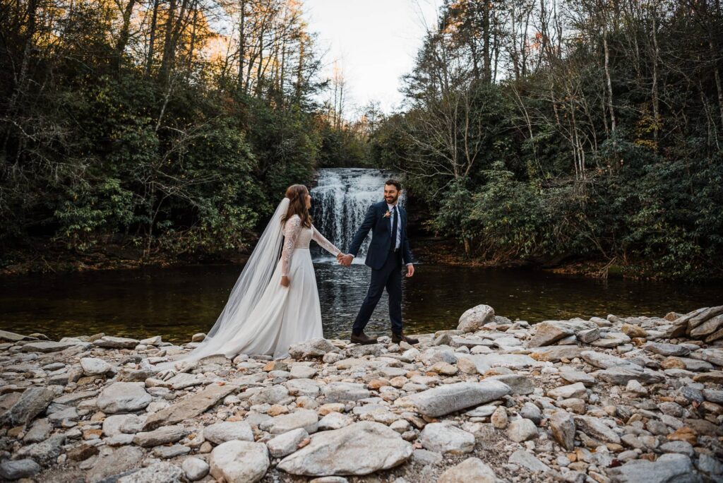 Couple walking in front of a waterfall in Nantahala National Forest after eloping.